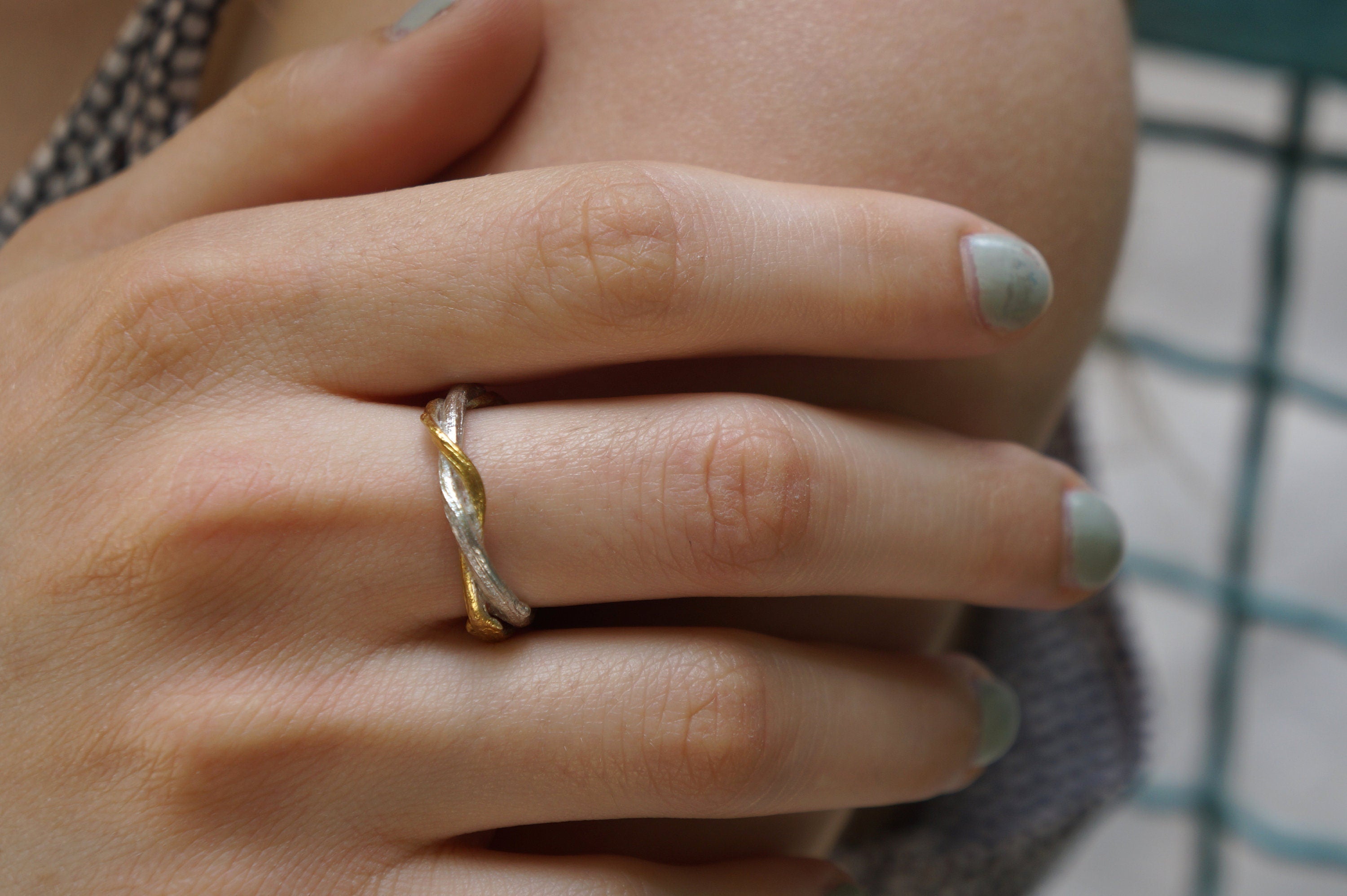 A close-up of a person's hand wearing a gold and silver ring on the ring finger.