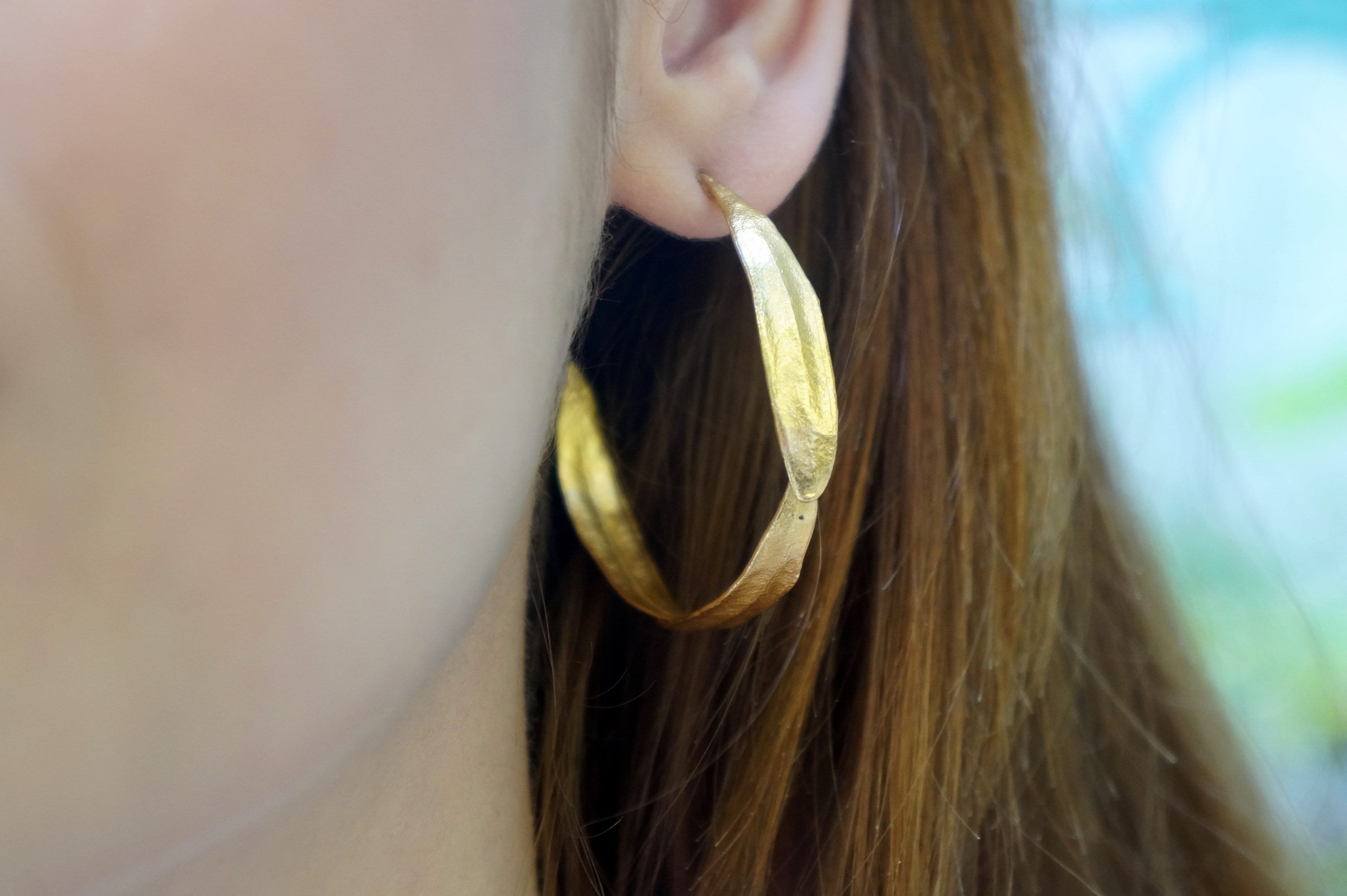 A close-up view of a person's ear adorned with a gold hoop earring.