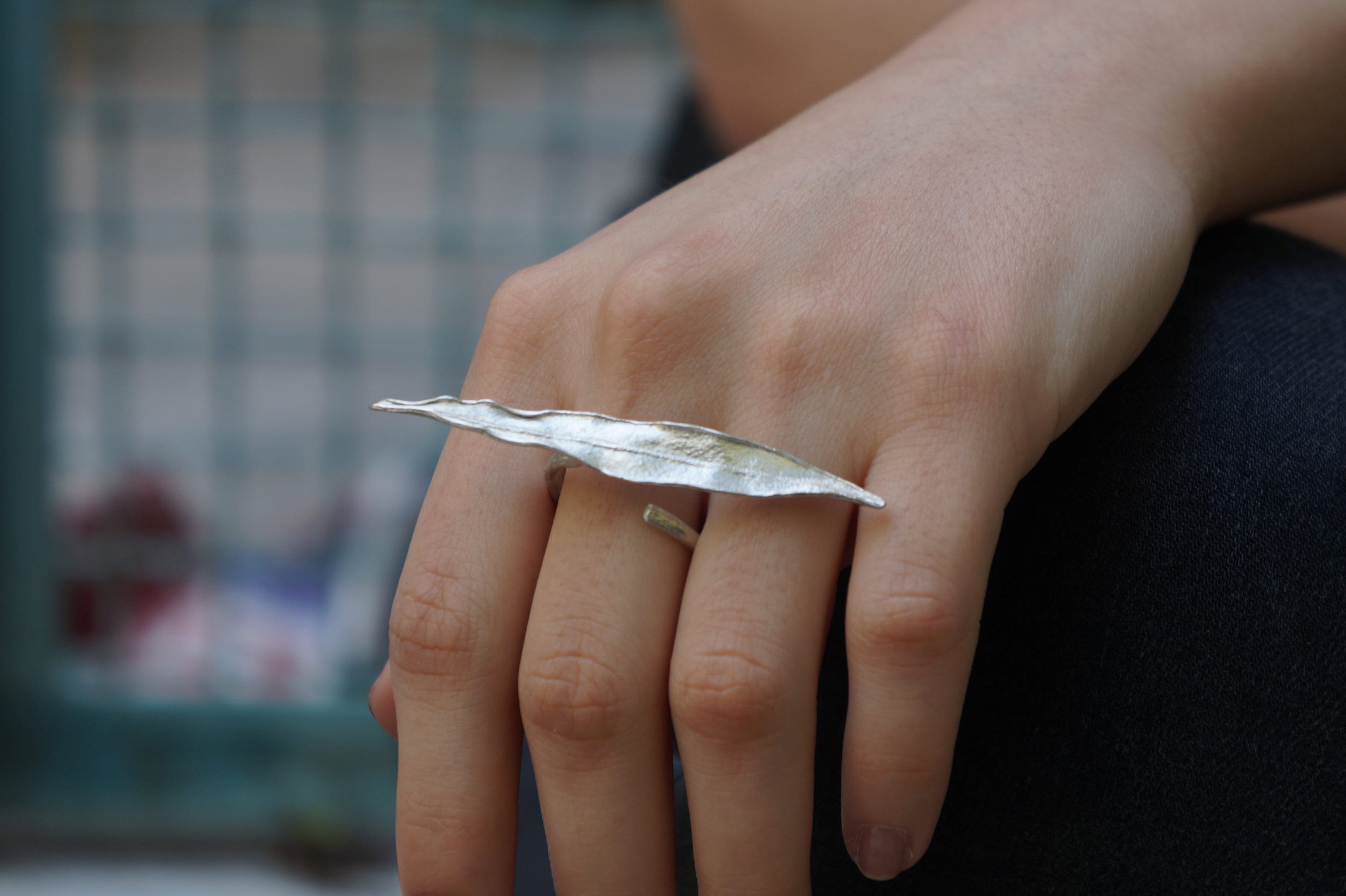 A close-up image of a person's hand wearing a silver leaf-shaped ring.