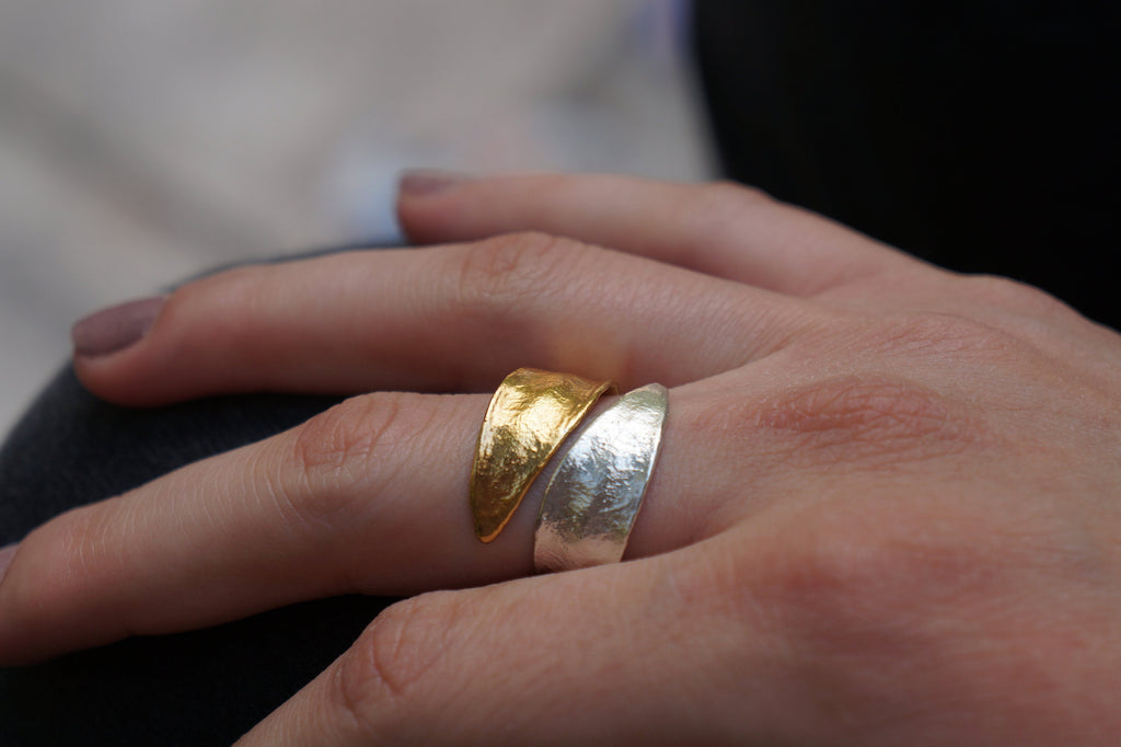 A close-up of a person's hand wearing two rings, one gold and one silver.
