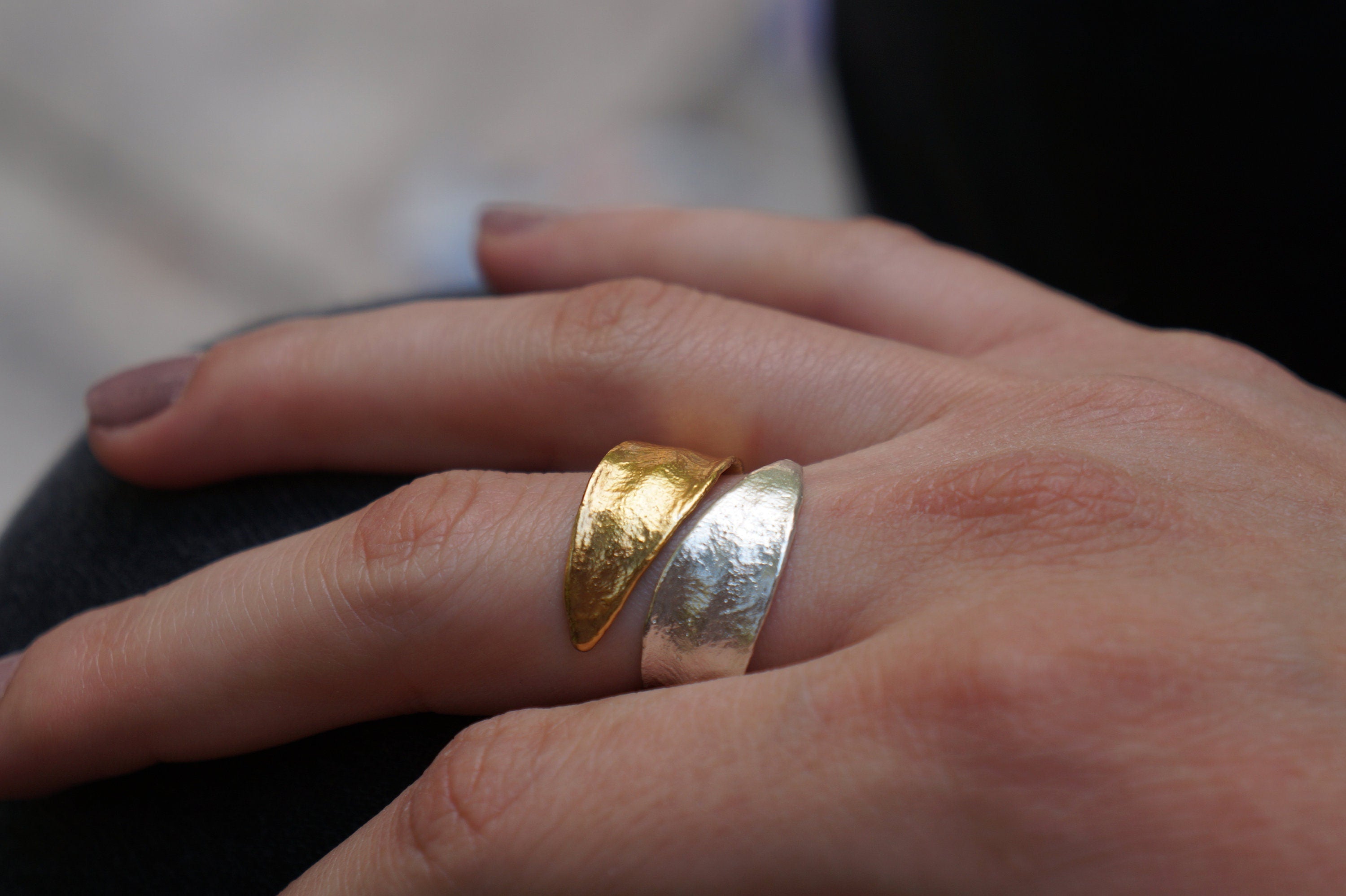 A close-up of a person's hand wearing two rings, one gold and one silver.