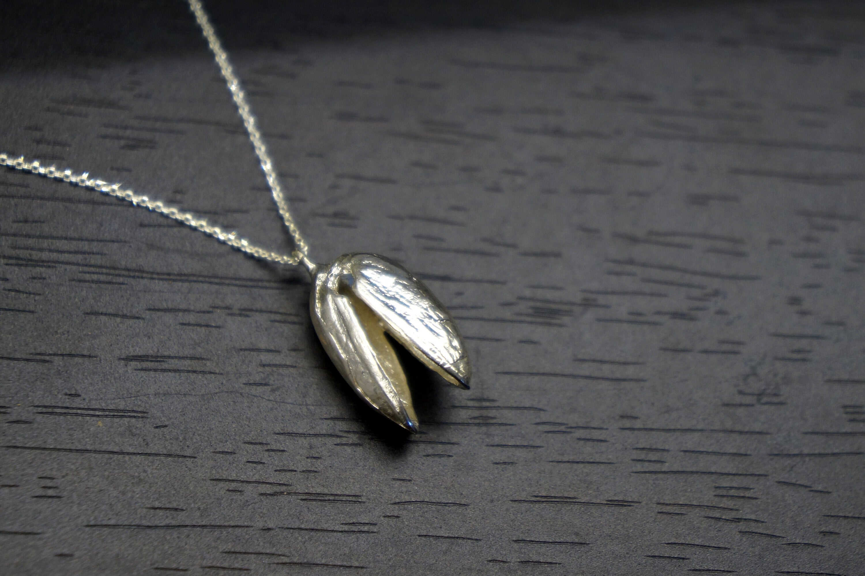 A silver necklace with a pendant in the shape of a flower is displayed on a dark surface.