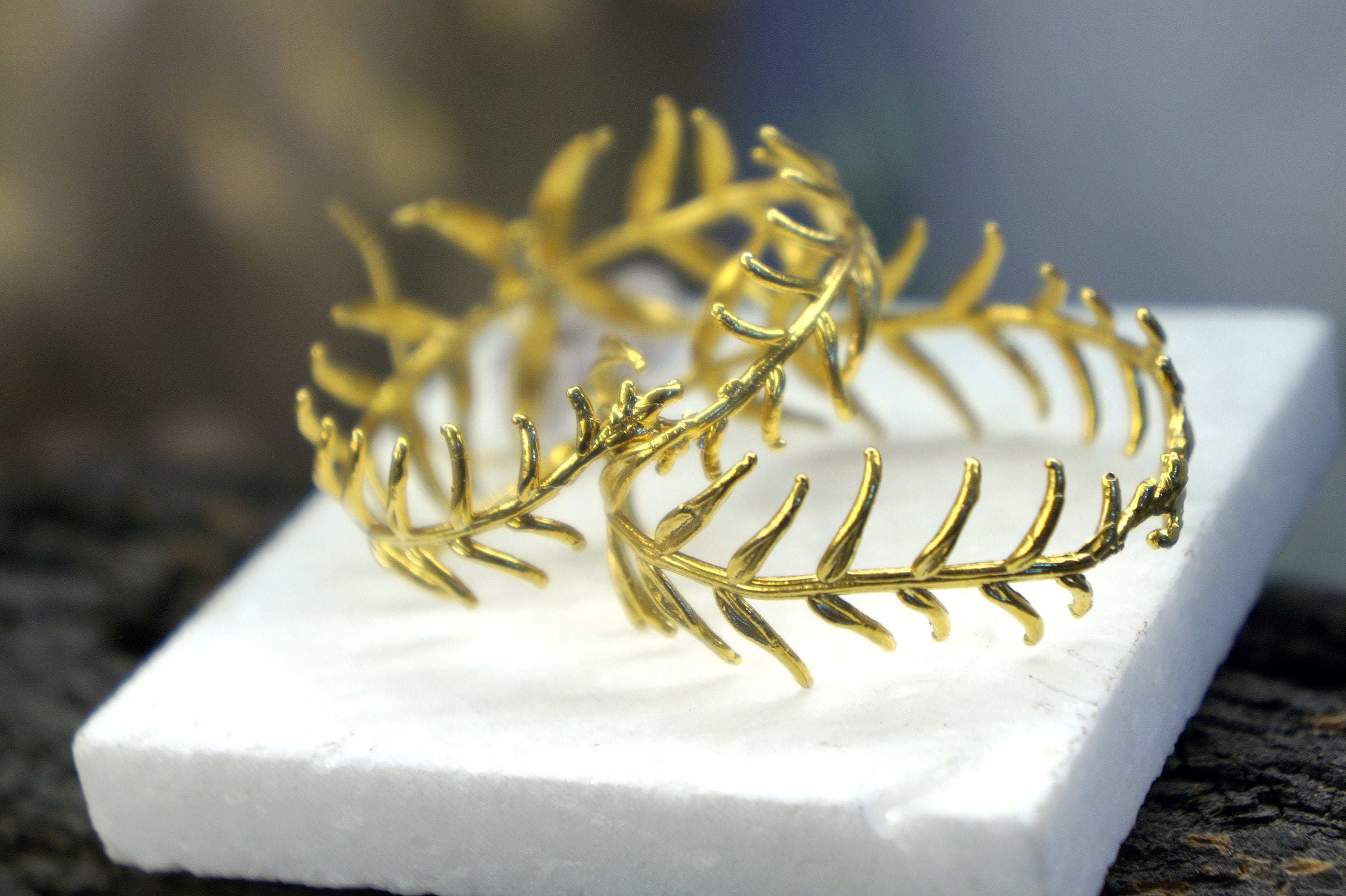 two gold leaf-like bracelets with intricate designs, resting on a white foam base.