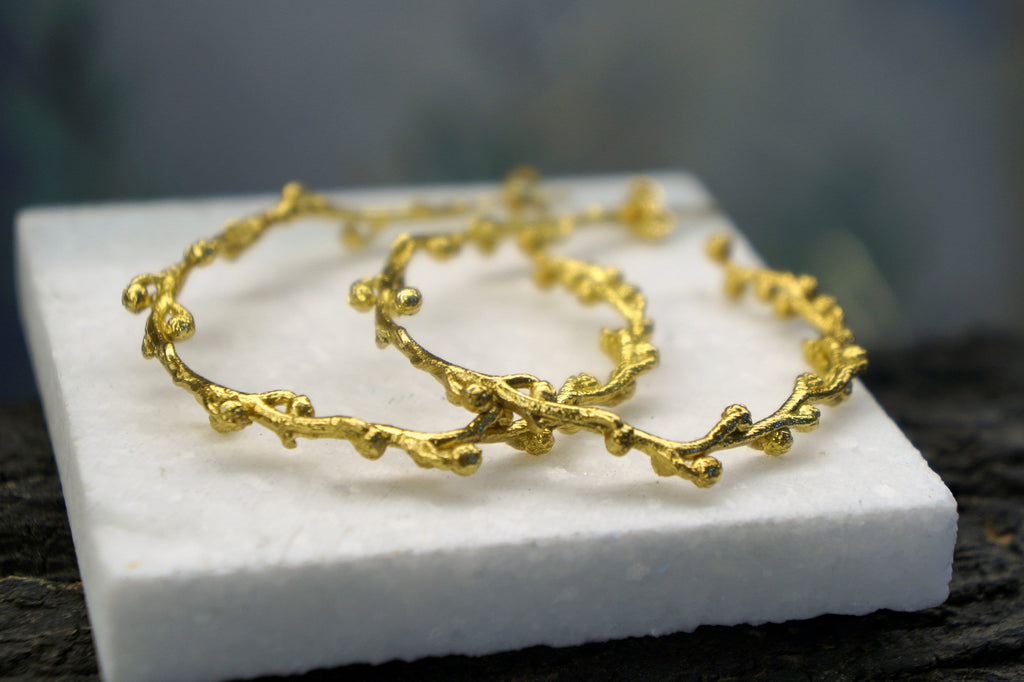 a pair of gold-colored bracelets with intricate designs, resting on a white surface.