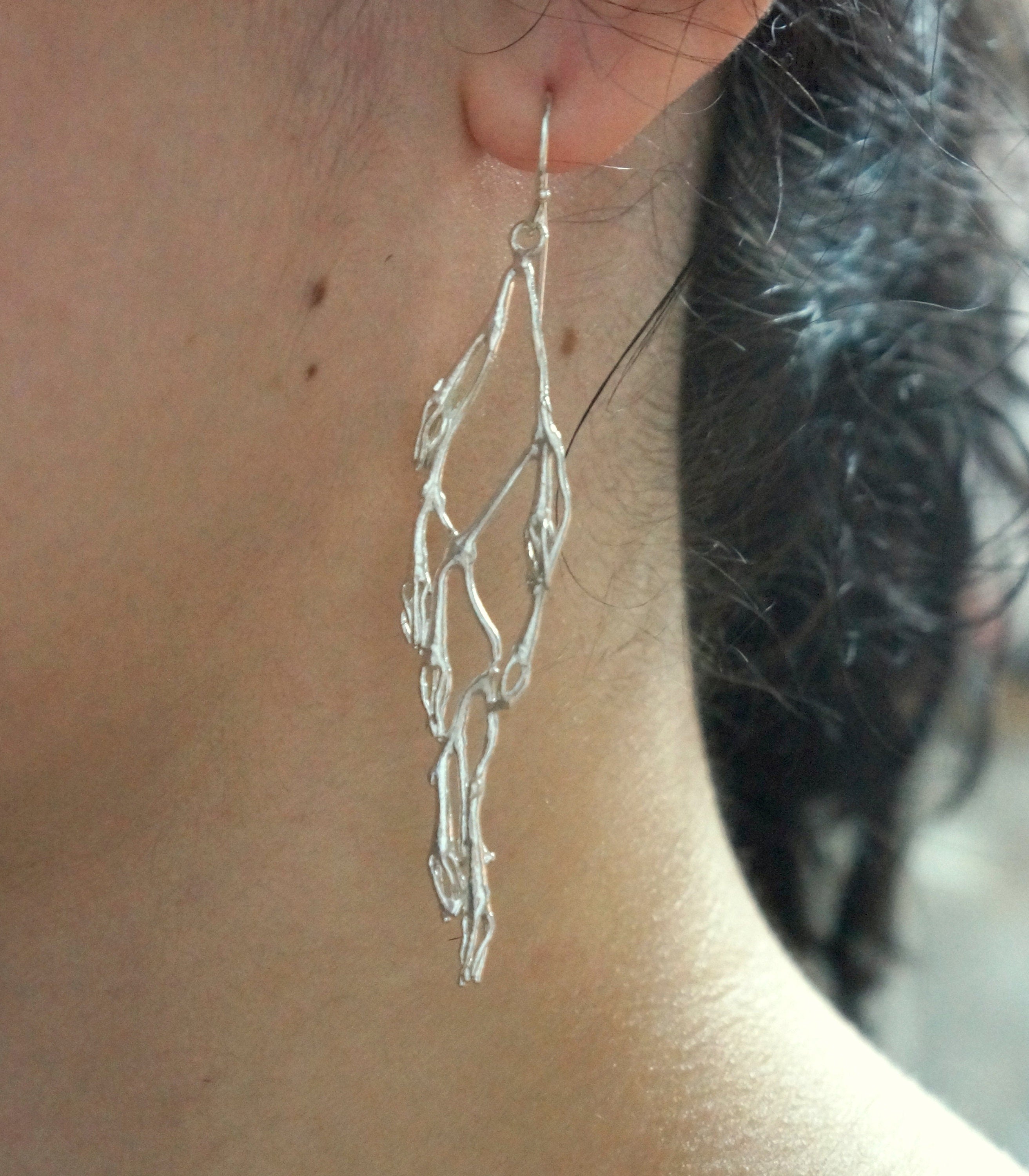 A close-up view of a person's ear wearing a silver earring with a delicate, leaf-like design.