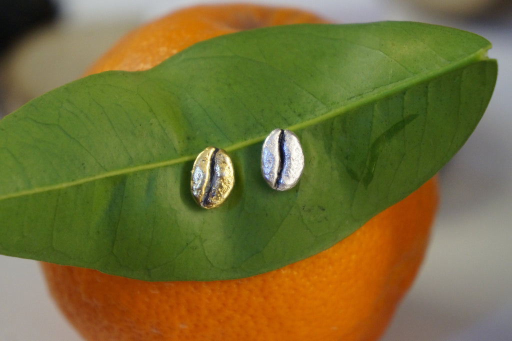 Two coffee beans are resting on a green leaf, which is placed on top of an orange fruit.