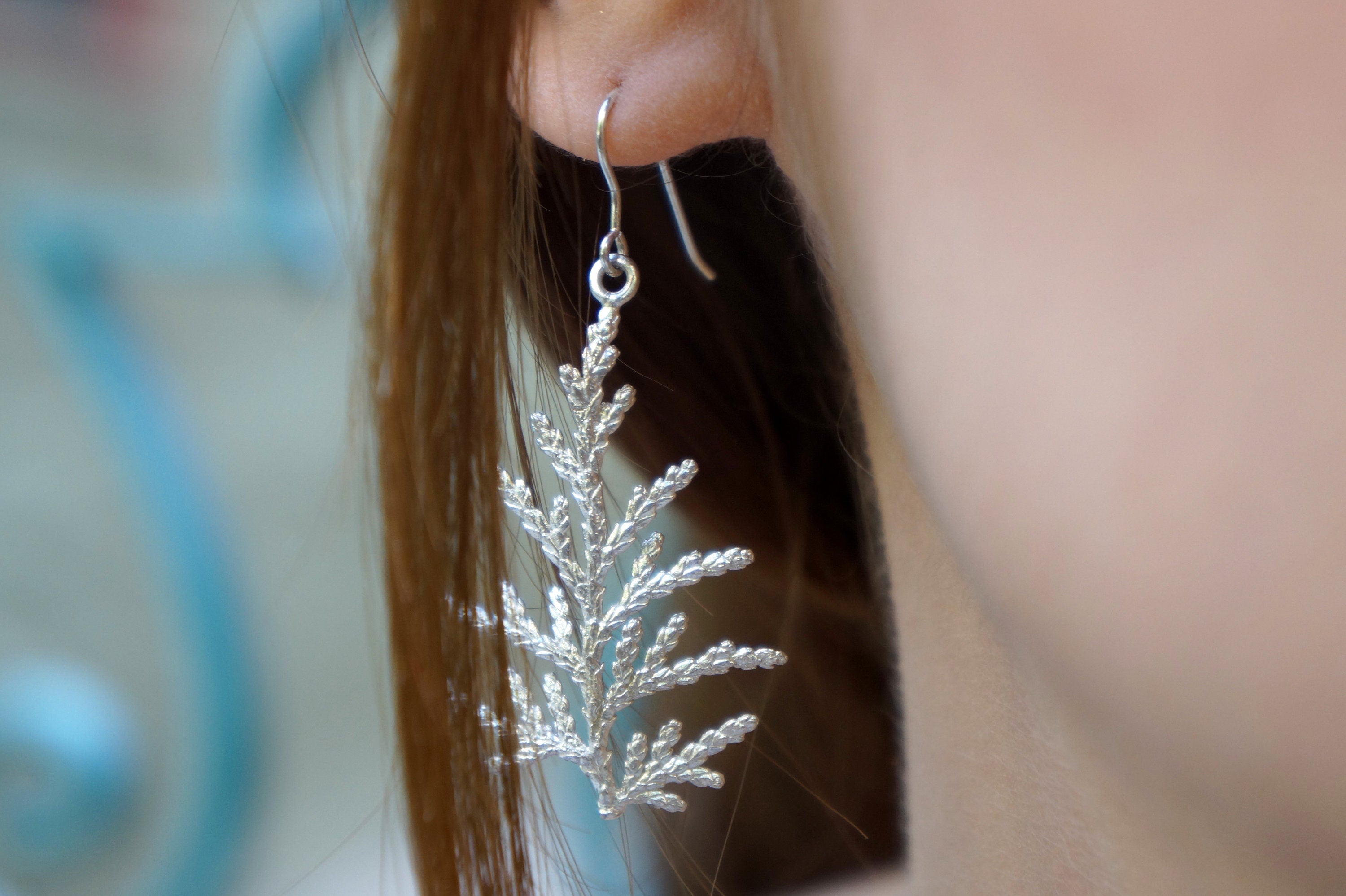 A close-up view of a person's ear wearing a silver earring shaped like a leaf or branch.