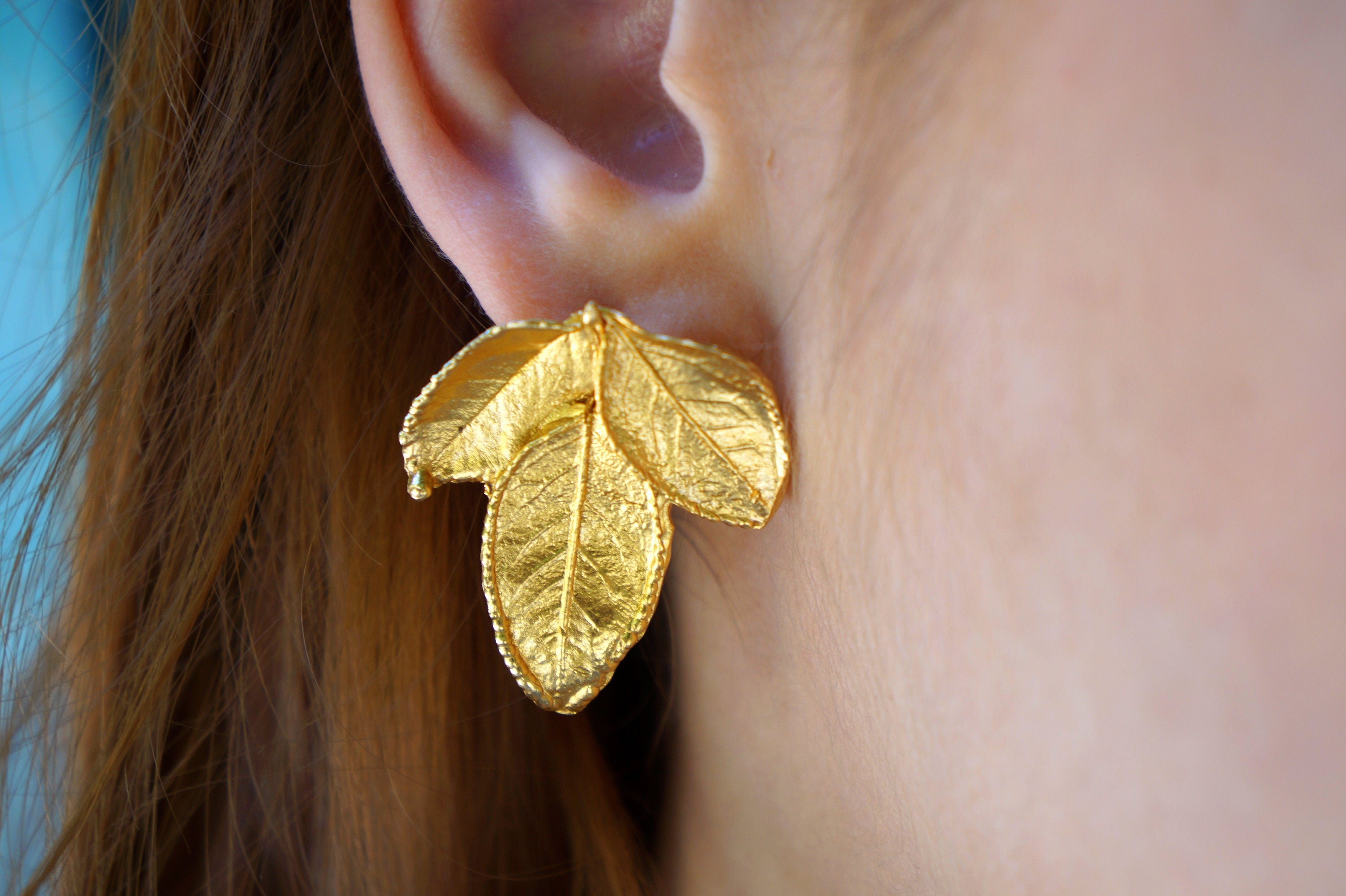 A close-up view of a person's ear adorned with a gold leaf earring.