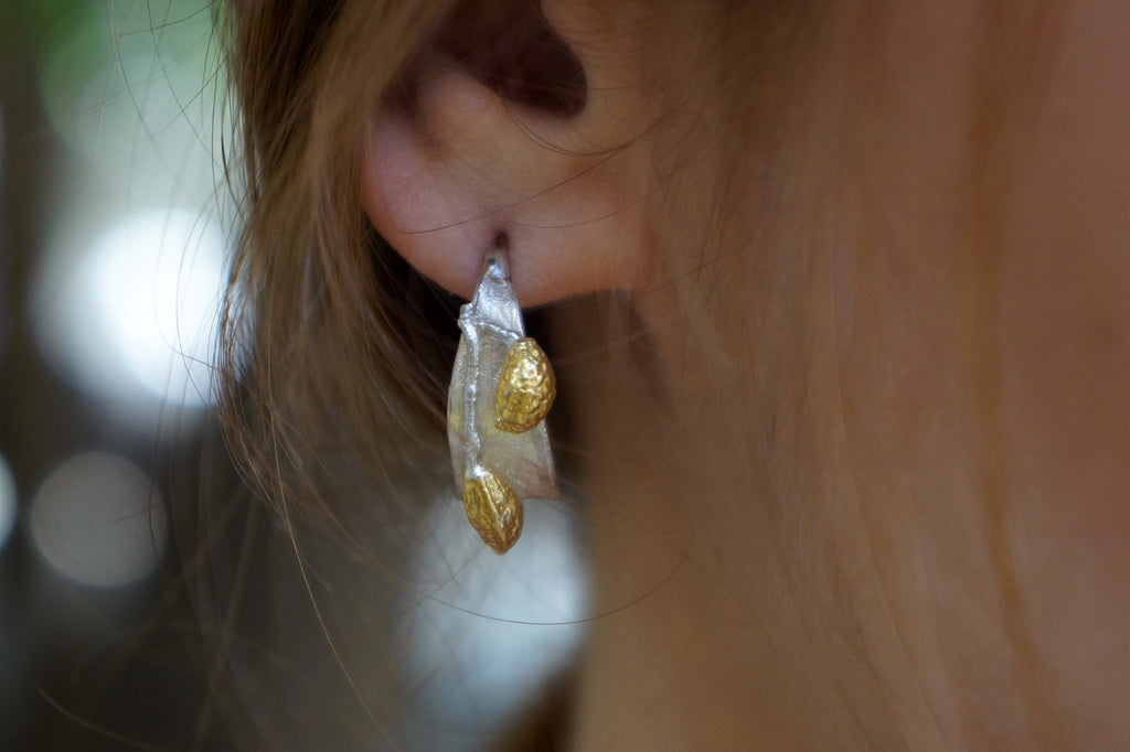 A close-up view of a person's ear adorned with a pair of earrings featuring two gold-colored almonds.