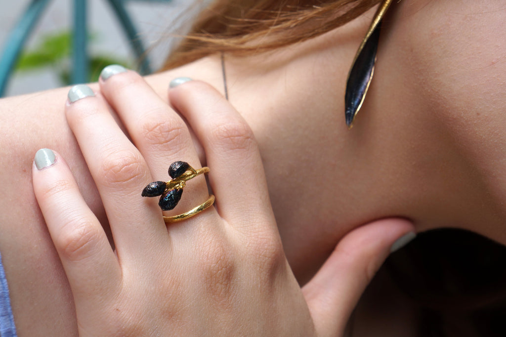 A close-up of a person's hand wearing a gold ring with black stones, and a gold earring with a black stone.