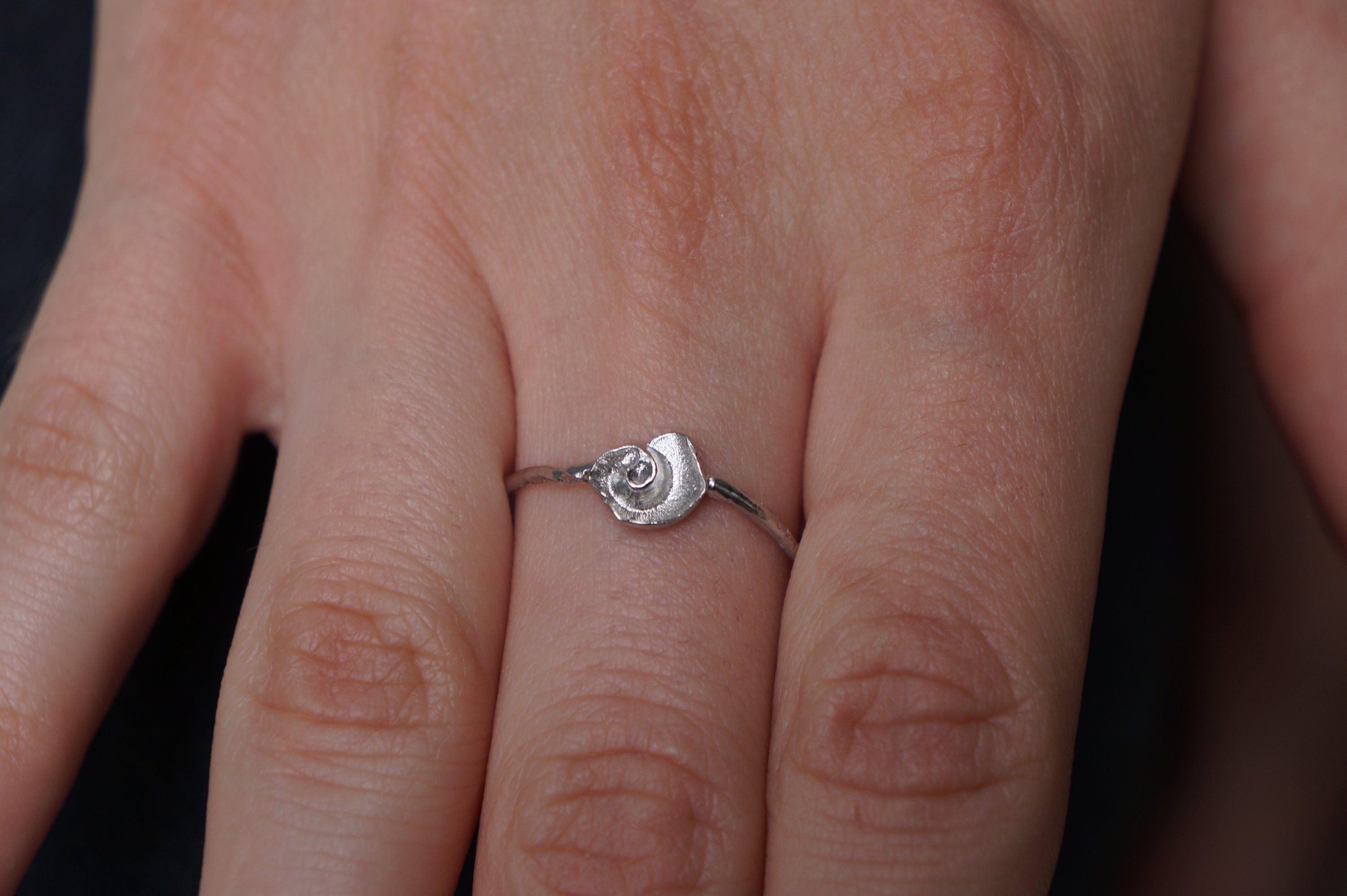 A close-up view of a person's hand wearing a silver ring with a small, intricately designed shell or flower-like object.
