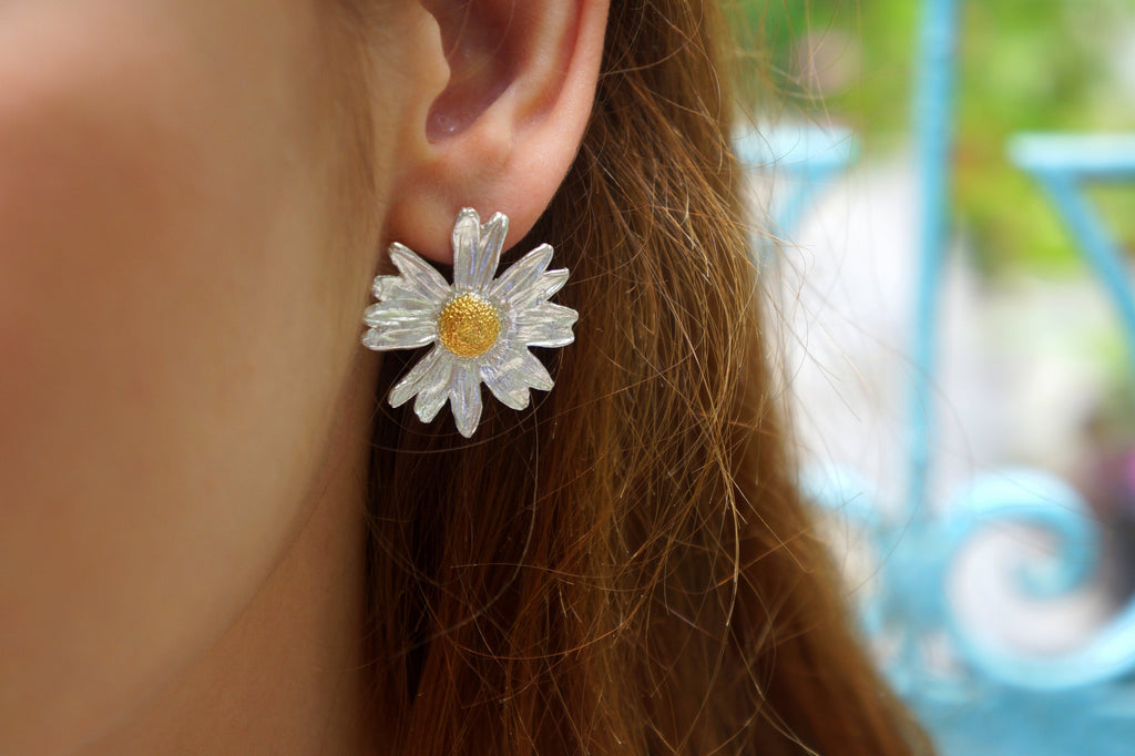 A close-up view of a person's ear adorned with a large, intricately designed earring featuring a white daisy flower.