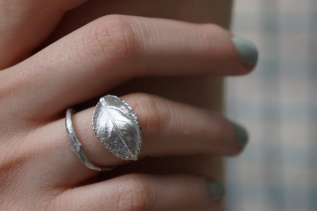 A close-up view of a silver leaf-shaped ring on a person's finger.