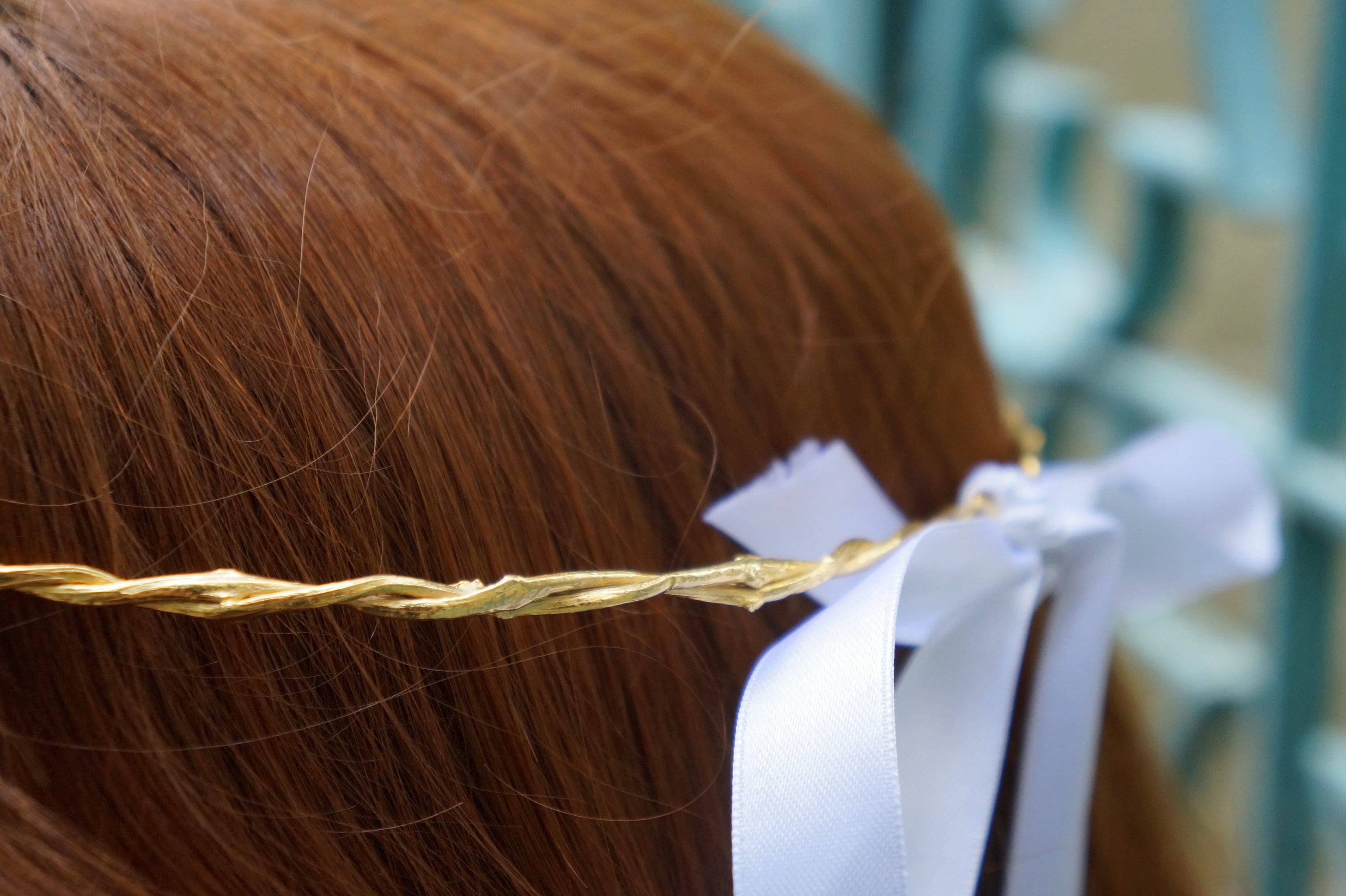 A close-up view of a person's head with a gold-colored ribbon tied around their hair.