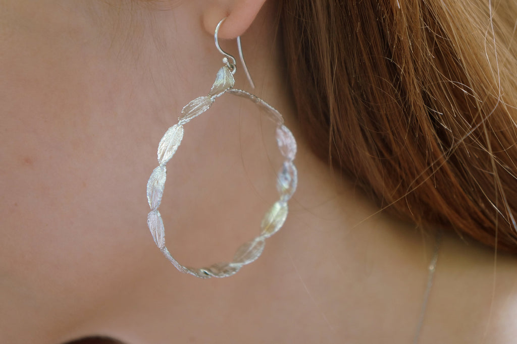 A close-up view of a person's ear wearing a silver hoop earring with leaf-shaped designs.