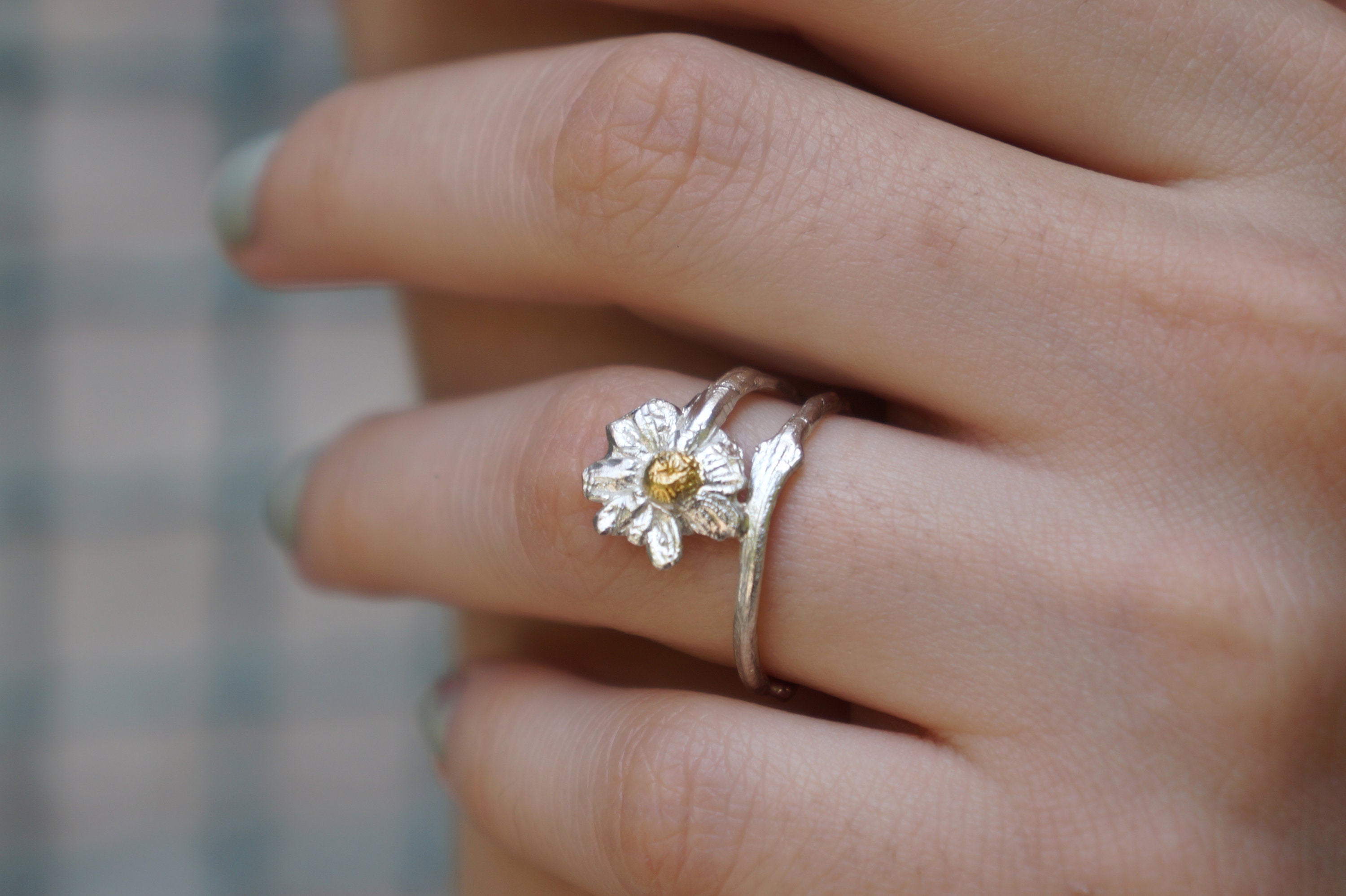 A close-up of a person's hand wearing a silver ring with a flower design.