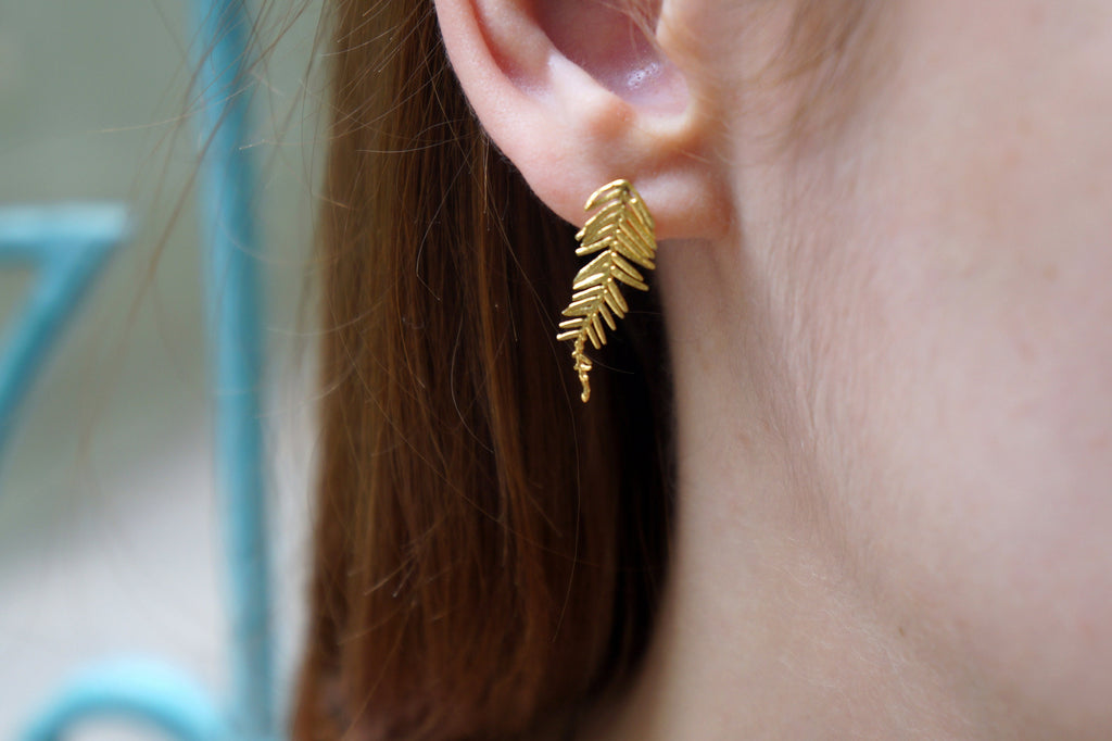 A close-up view of a person's ear wearing a gold leaf earring.