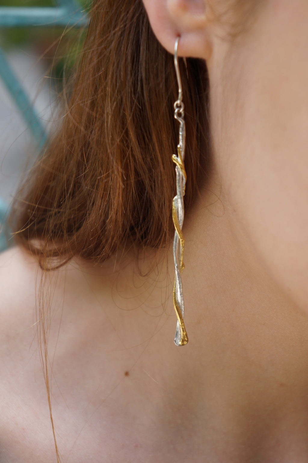 A close-up view of a person's ear wearing a pair of dangling earrings with a twisted, metallic design.
