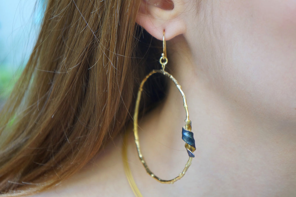A close-up view of a person's ear wearing a gold hoop earring with a blue and gold spiral design.