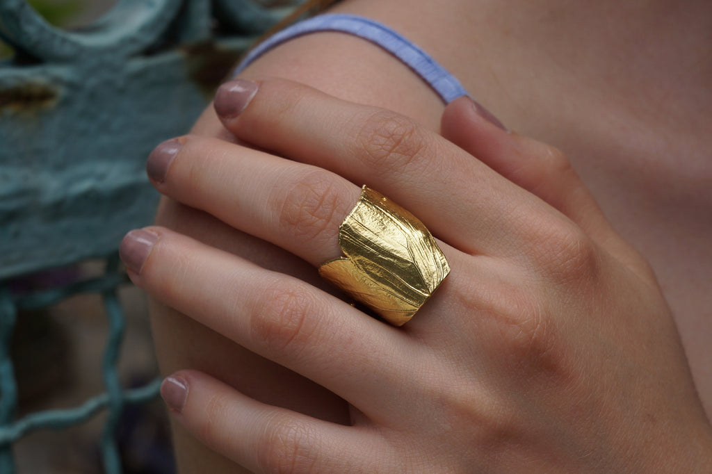 A close-up of a person's hand wearing a gold leaf ring on the ring finger.