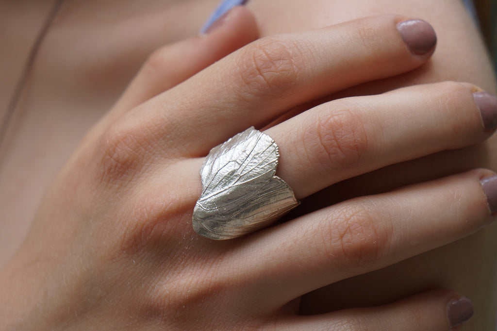 A close-up image of a person's hand wearing a silver leaf-shaped ring.