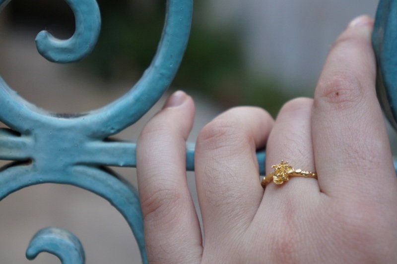 A close-up of a hand wearing a gold ring with a small flower design, resting on a blue metal gate.