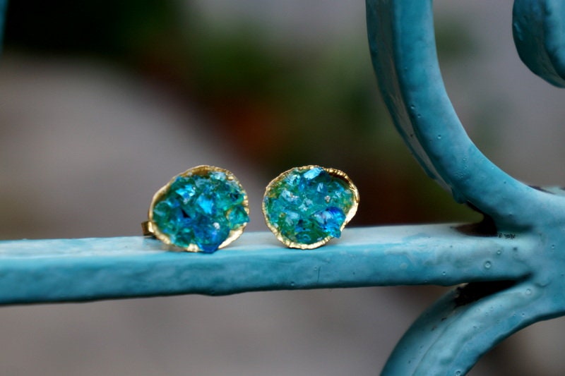 a pair of gold earrings with blue gemstones, placed on a blue metal railing.