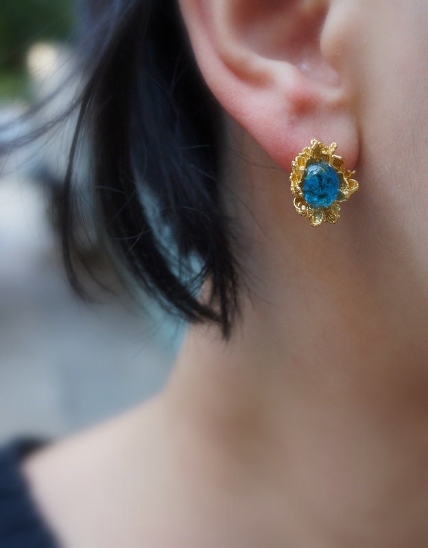 A close-up view of a person's ear wearing a gold earring with a blue gemstone.