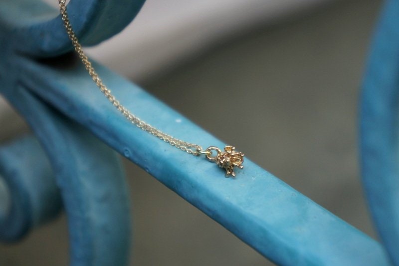 A delicate gold-colored necklace with a small pendant is resting on a blue metal surface.