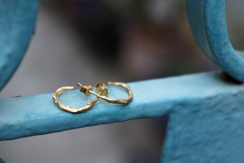 A pair of gold hoop earrings with a textured design rests on a blue metal surface.