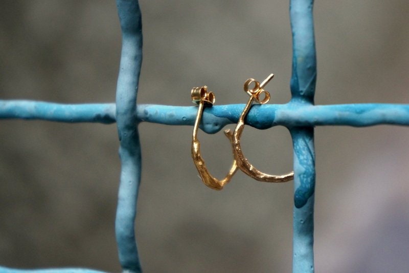 A pair of gold hoop earrings is hanging from a blue metal fence.