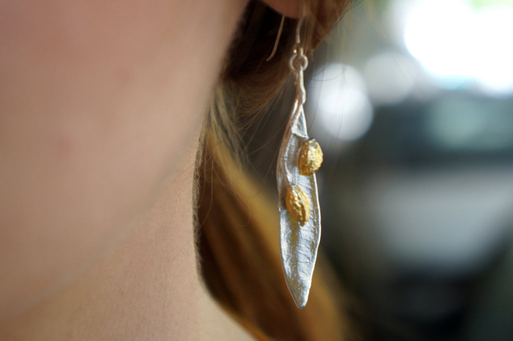 A close-up view of a person's ear wearing a silver earring with a leaf-like design and two small gold-colored stones.