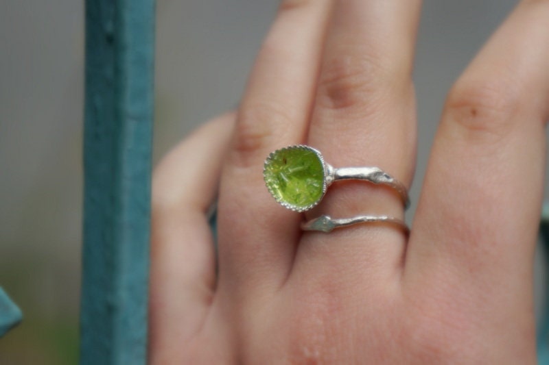 A close-up of a person's hand wearing a silver ring with a green gemstone, and another ring on the same hand.