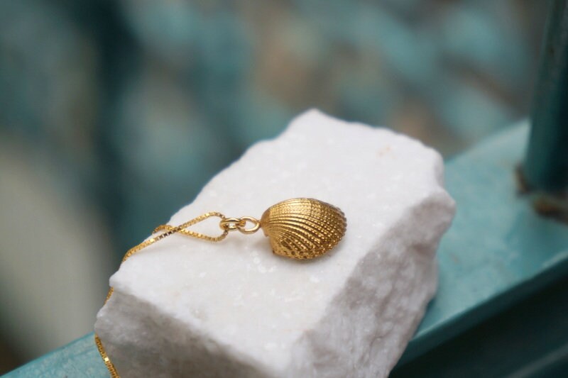 A gold necklace with a shell pendant is resting on a white marble surface.