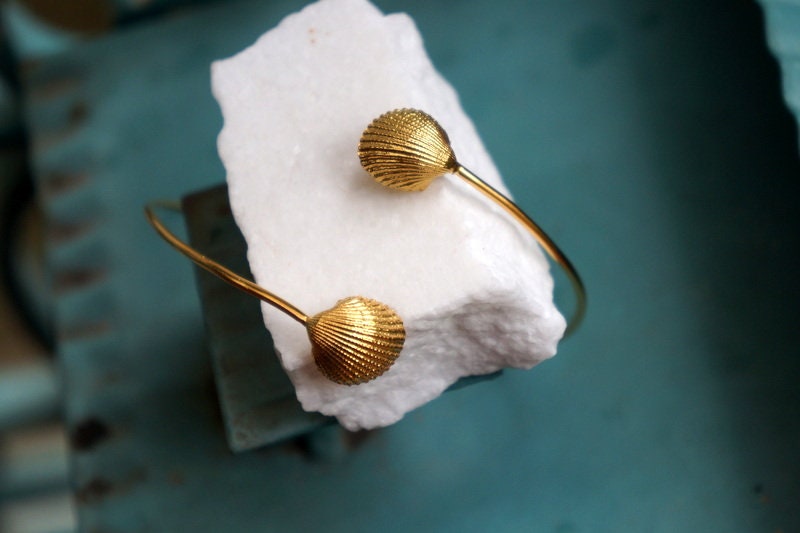 A pair of gold-colored shell-shaped bracelets resting on a white marble surface.