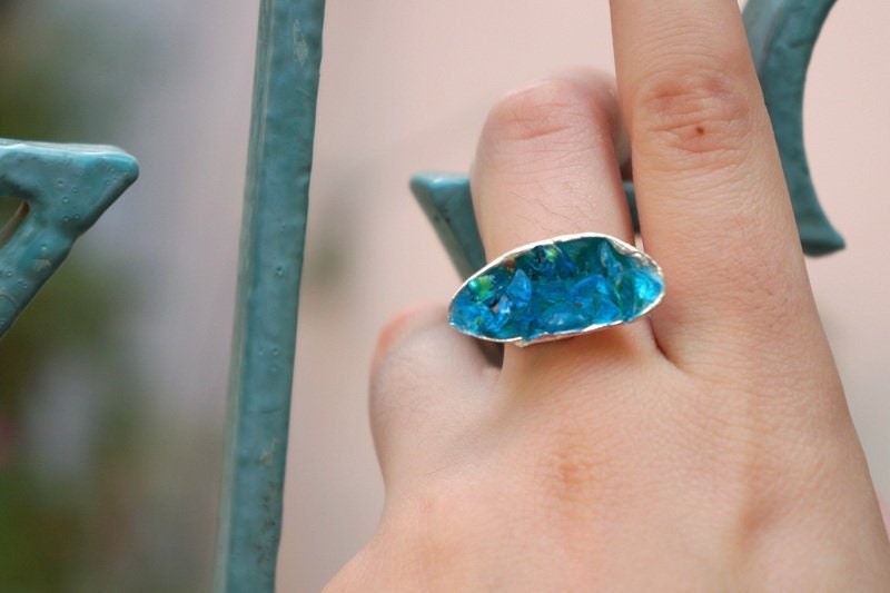 A close-up of a hand wearing a ring with a blue gemstone, held up against a blurred background.