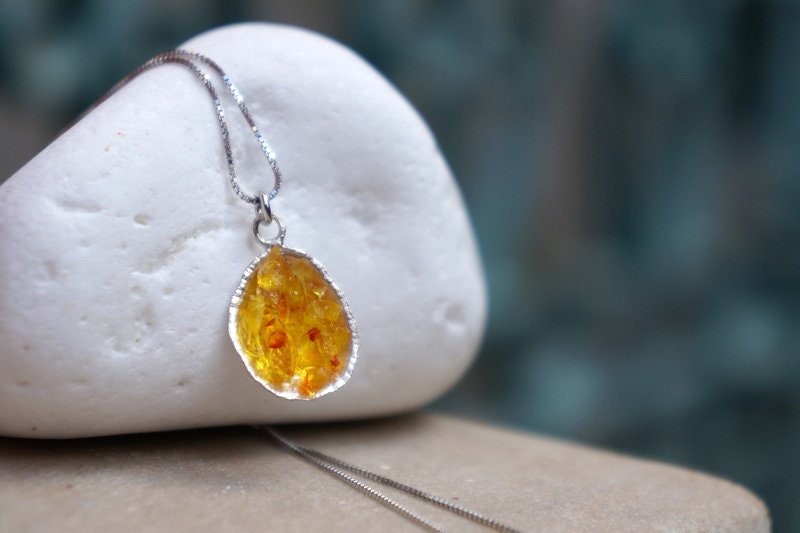 A necklace with a pendant made of a yellowish-orange stone is displayed on a white rock.