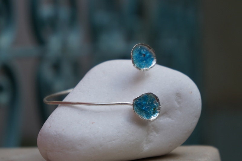 A silver bracelet with blue gemstones is resting on a white rock.