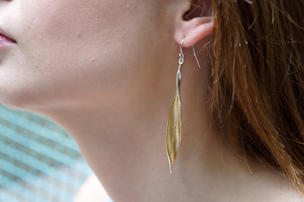 A close-up of a person's ear wearing a pair of gold leaf earrings.
