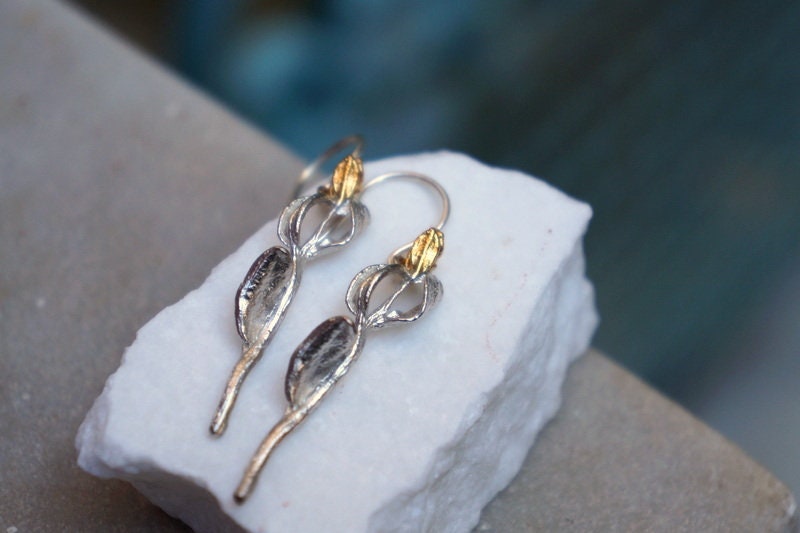 A pair of silver earrings with gold accents, featuring intricate designs, are displayed on a white marble surface.