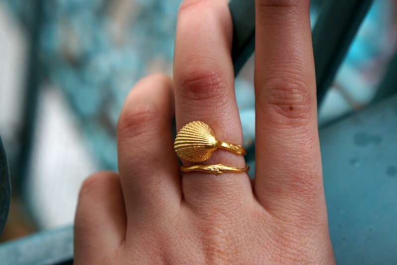 A close-up of a person's hand wearing a gold ring with a shell-shaped design.