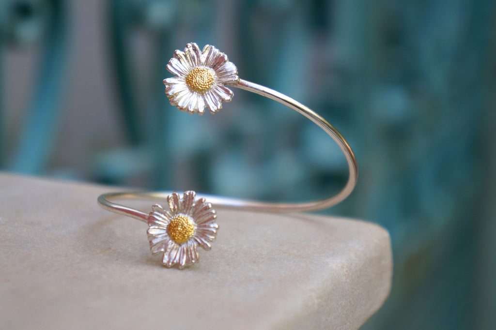 A silver bracelet with two white flower-shaped charms on a beige surface.