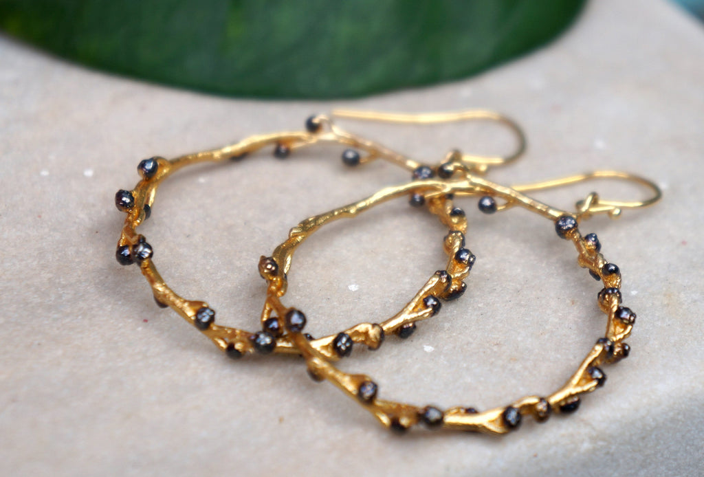 A pair of gold earrings with black gemstones, resting on a white surface.
