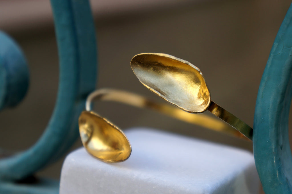 A close-up image of a gold-colored spoon-shaped bracelet on a white surface.