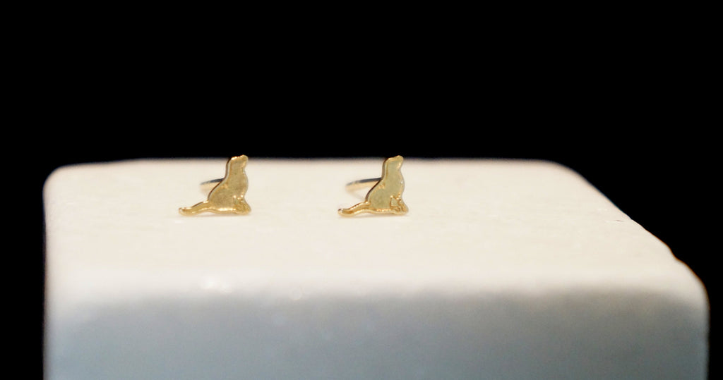 A pair of gold-colored earrings with a cat-like design, placed on a white surface against a black background.