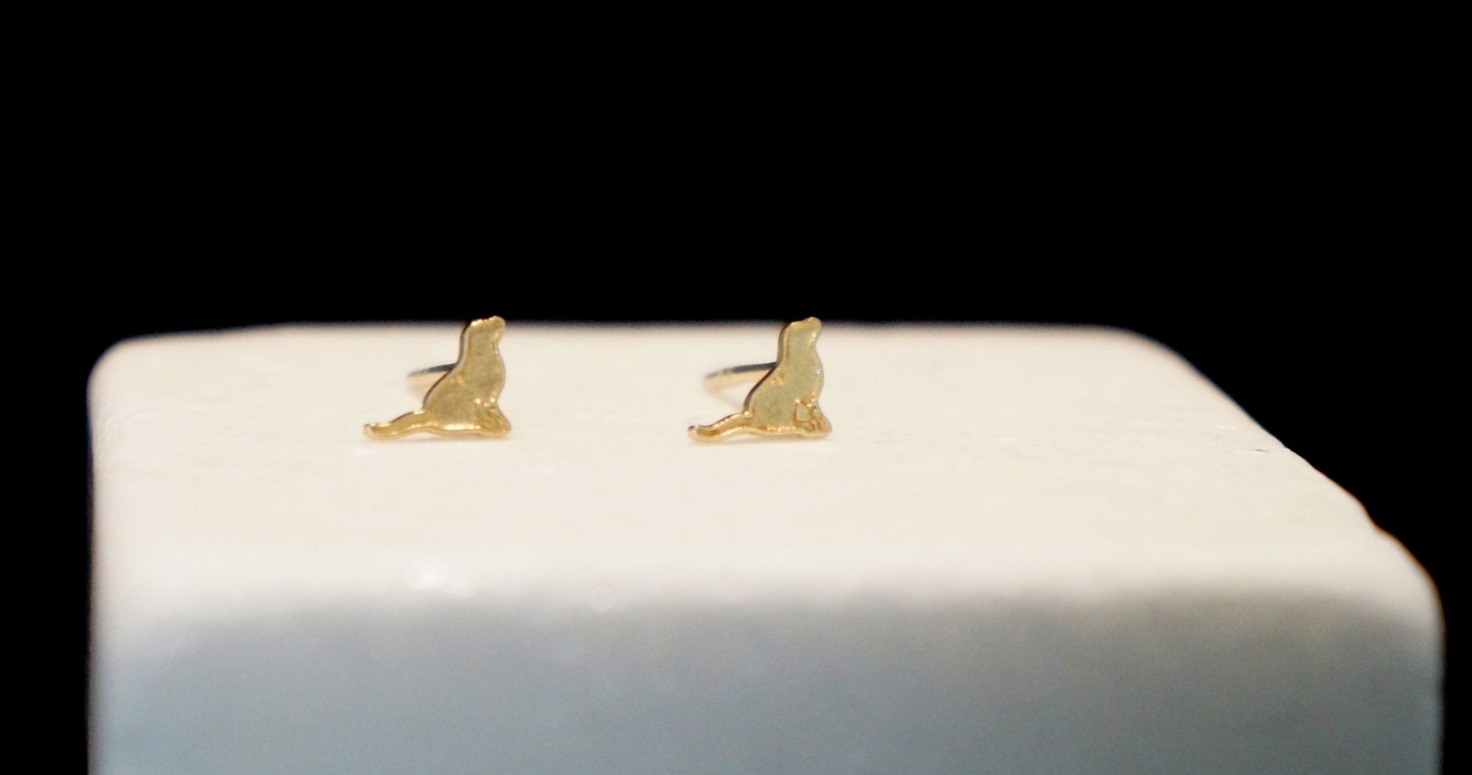 A pair of gold-colored earrings with a cat-like design, placed on a white surface against a black background.