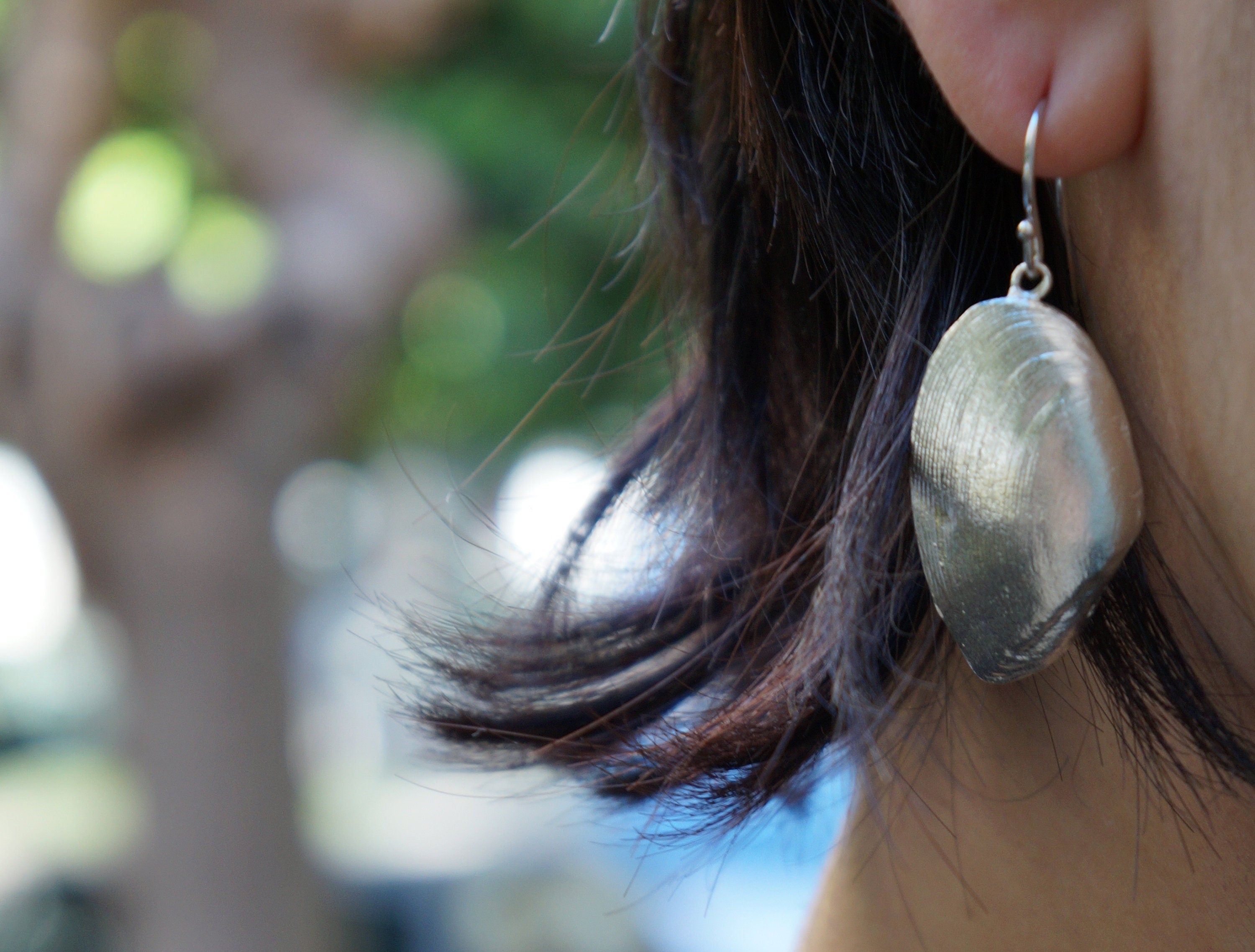 A close-up view of a person's ear wearing a silver shell-shaped earring.