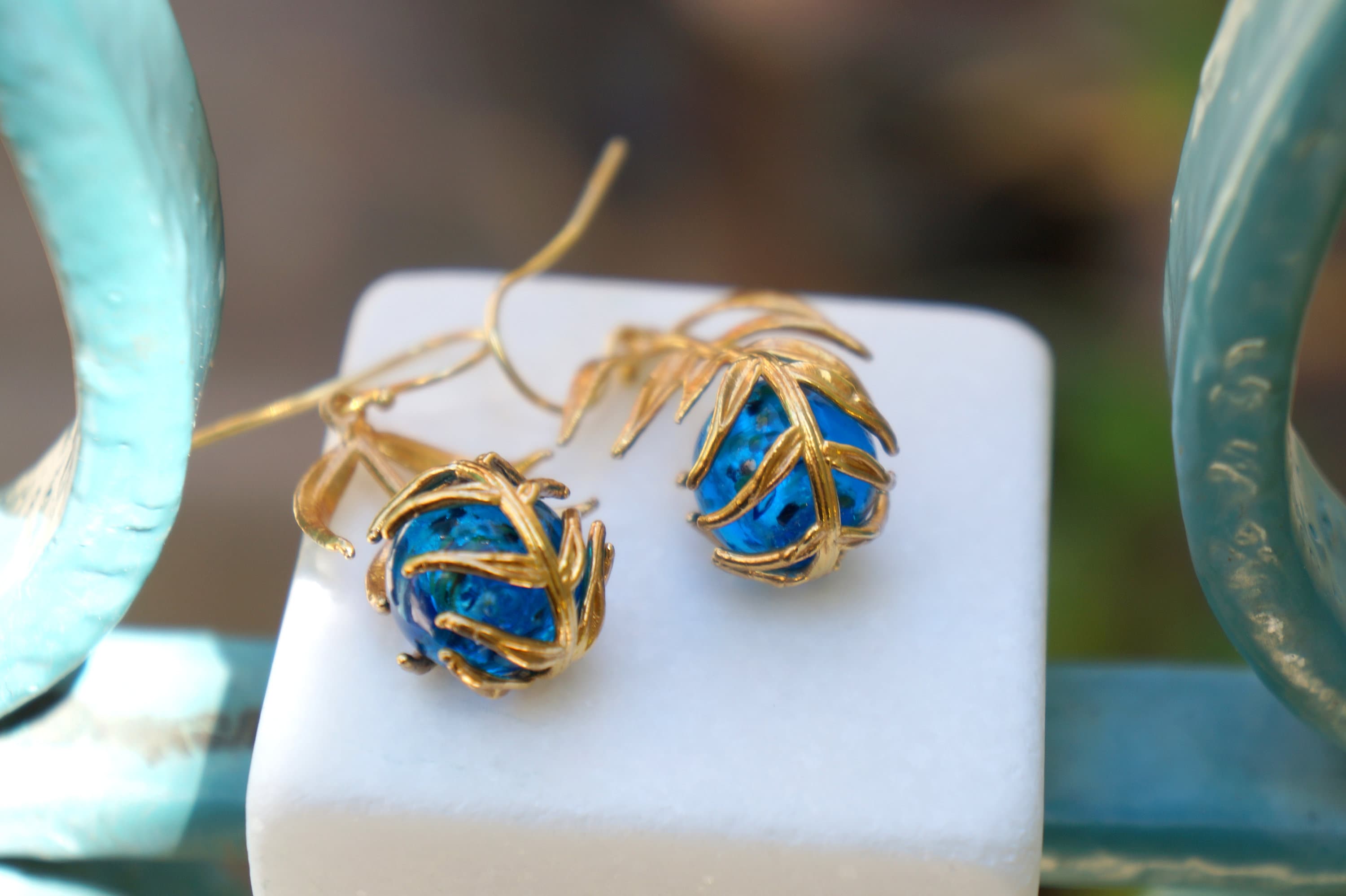A pair of gold-colored earrings with blue gemstones, placed on a white surface.