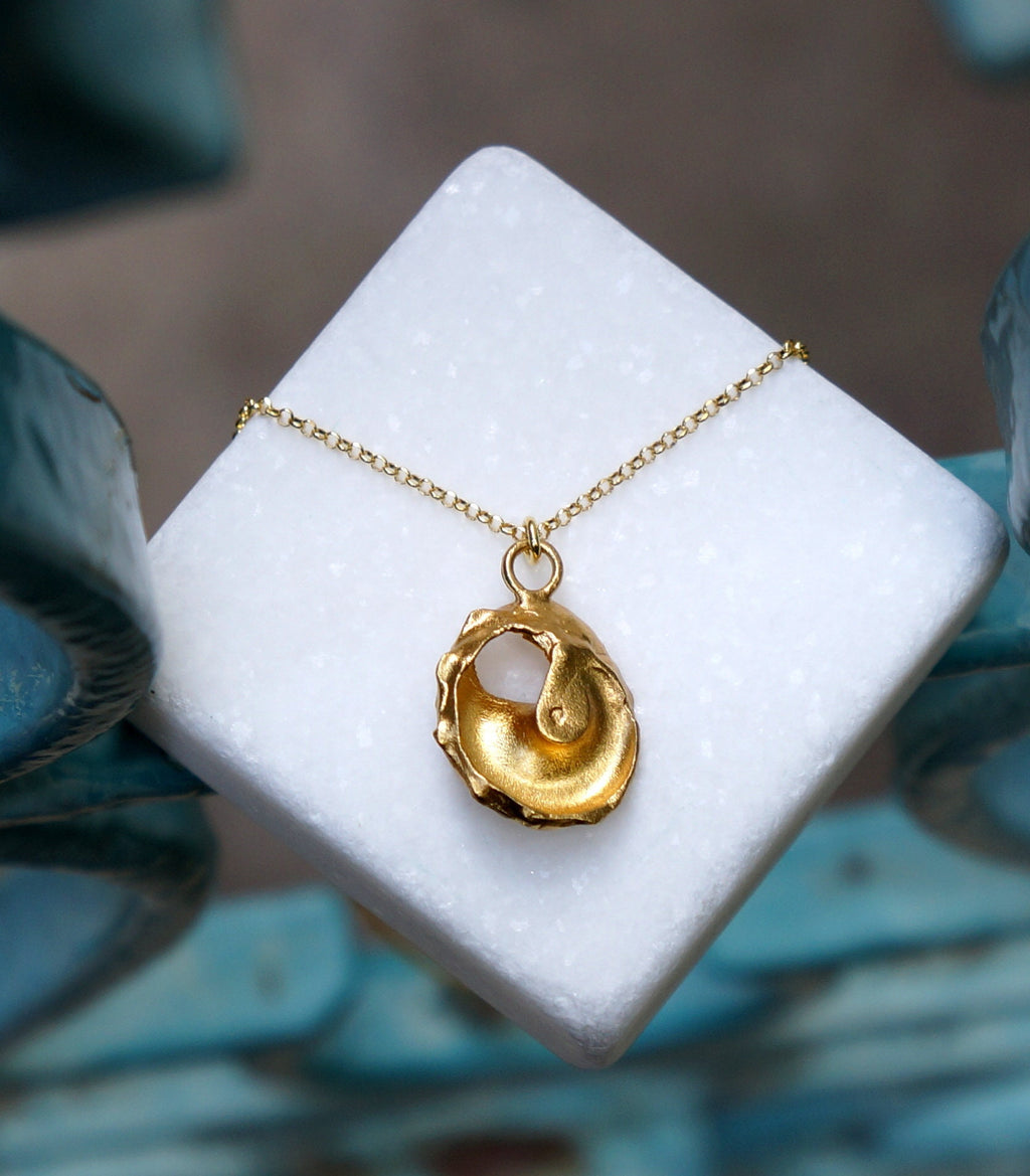 A gold necklace with a pendant in the shape of a shell rests on a white marble surface.