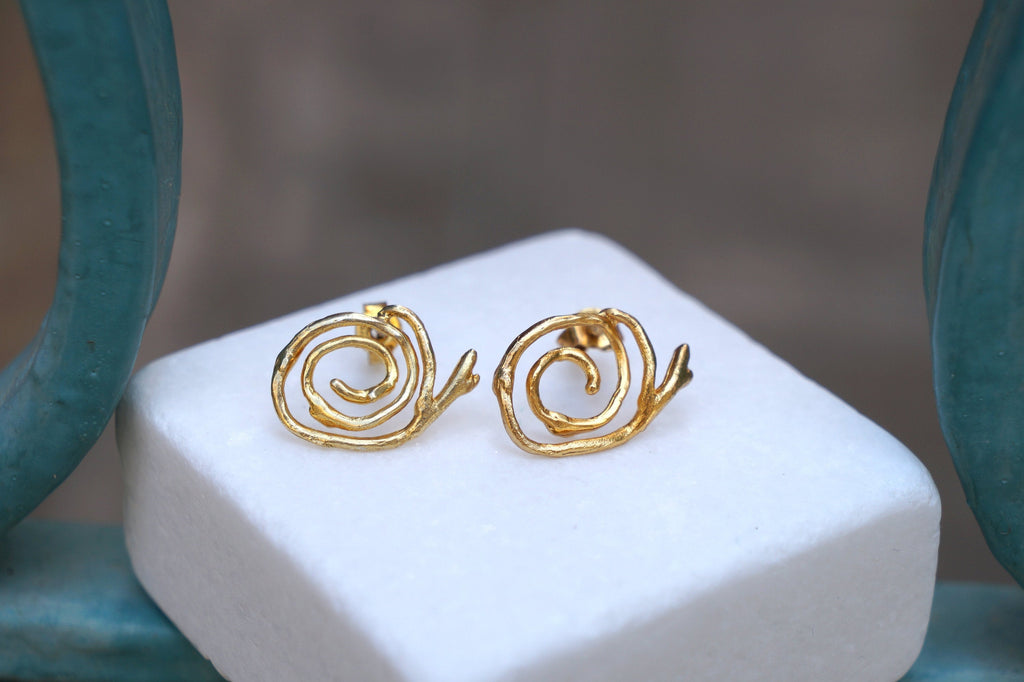 A pair of gold earrings with spiral designs, placed on a white surface.